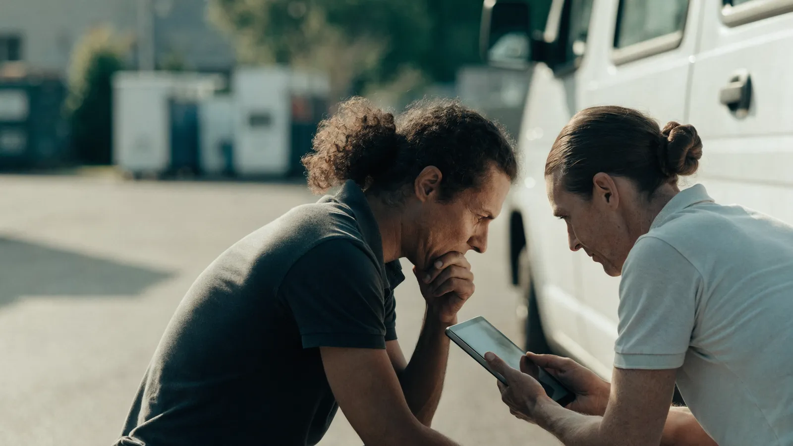 Two pest control operators crouched by a service van weighing software options on a tablet, choosing between an AI overlay and rip-and-replace.