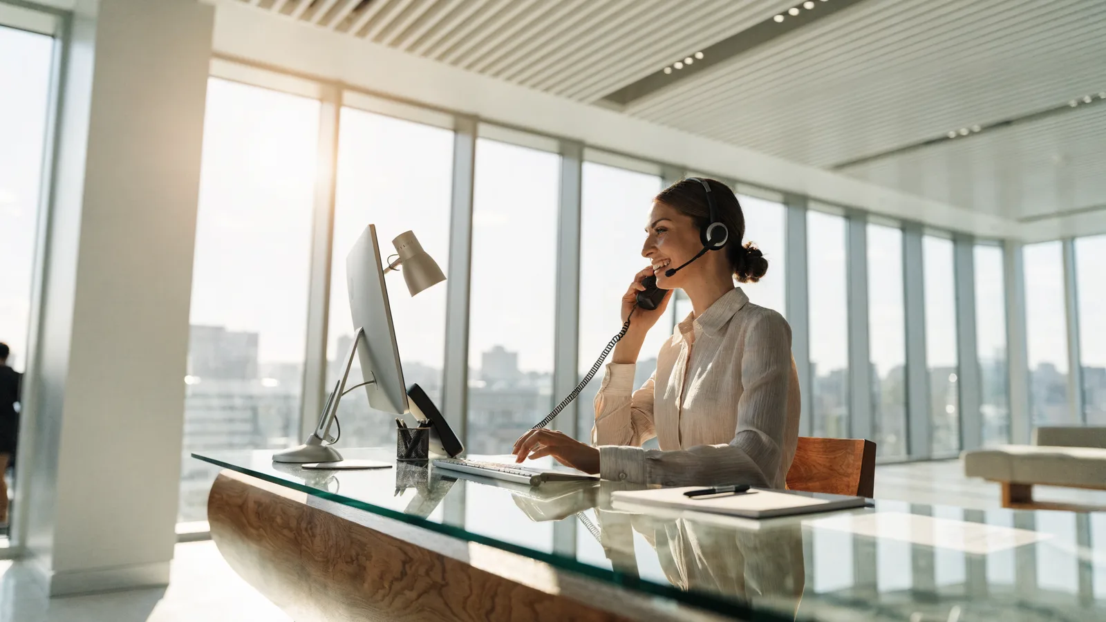 Smiling pest control receptionist in a telephone headset answering calls and booking appointments at a front-desk computer,