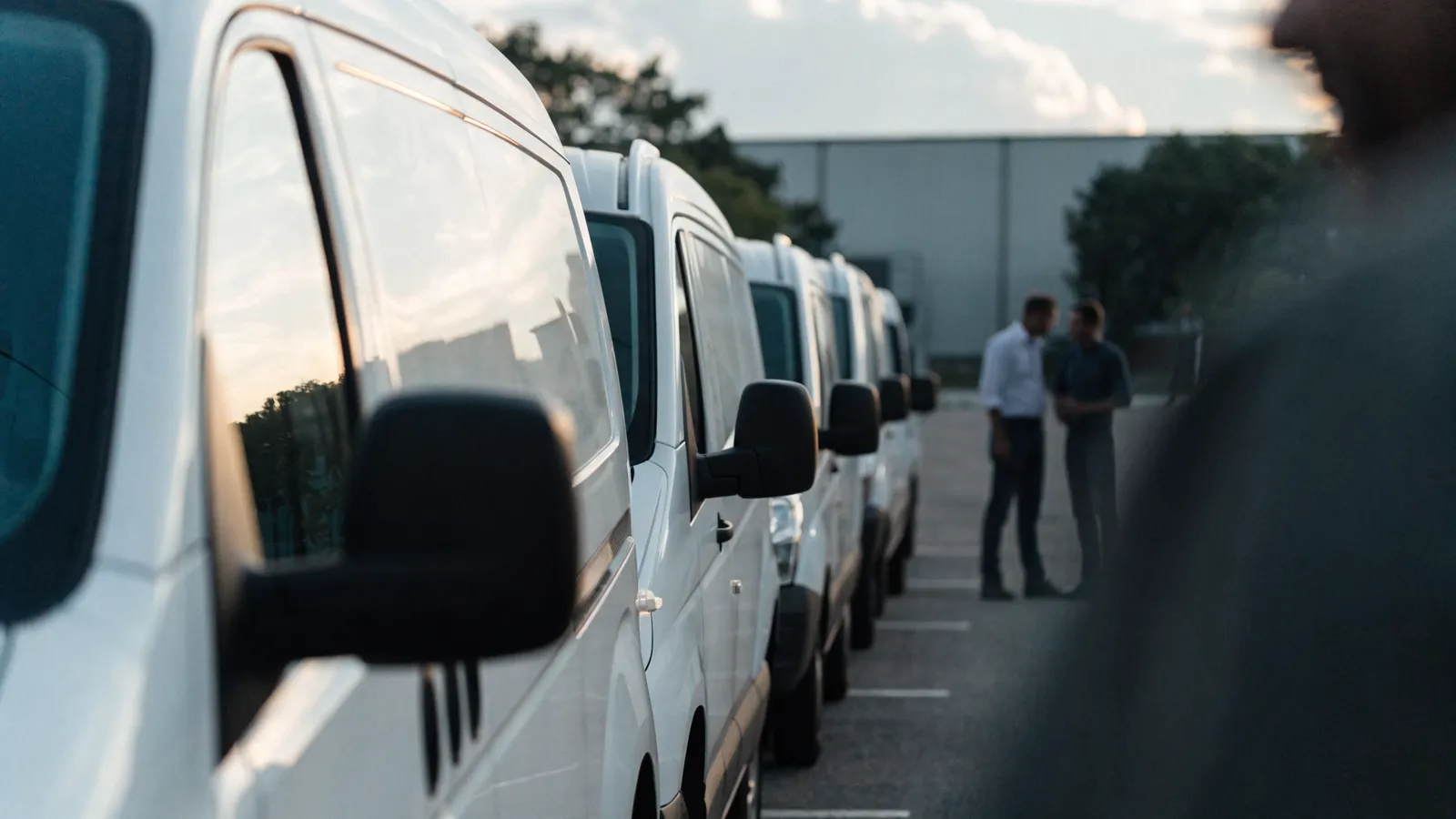 Photo of a row of white pest-control service vans lined up at a depot as two route managers discuss daily routing and dispatch plans.