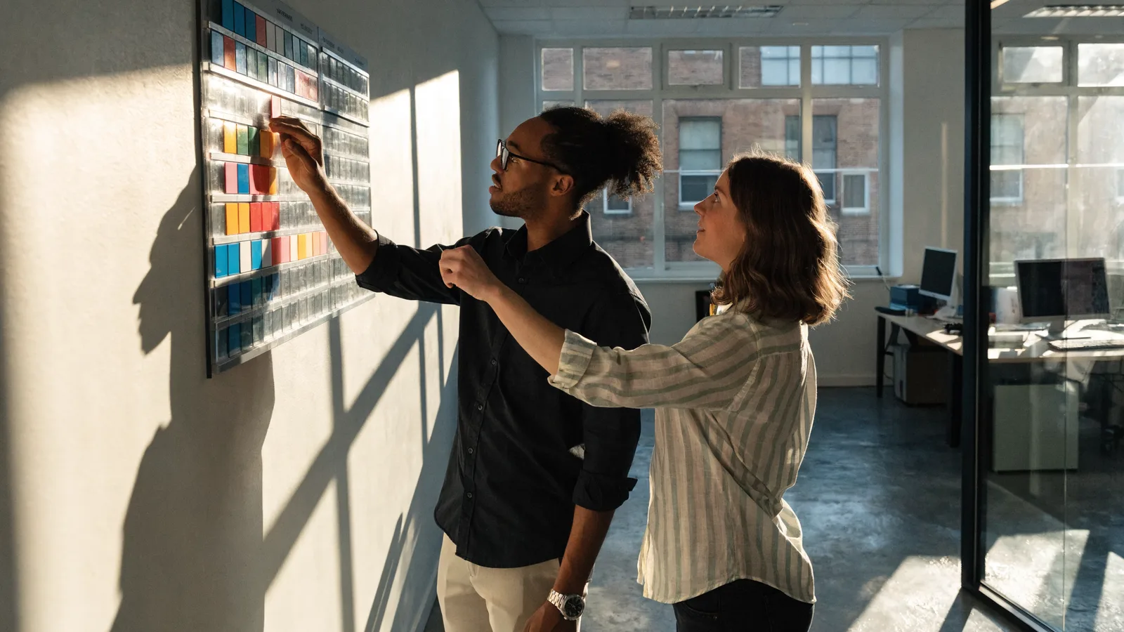 Photo of two pest-control operations planners arranging magnetic tiles on a wall scheduling board to map technician routes and recurring service appointments