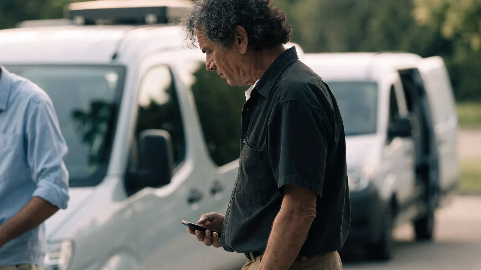Photo of a pest-control fleet owner checking his phone beside a row of service vans while weighing GorillaDesk alternatives